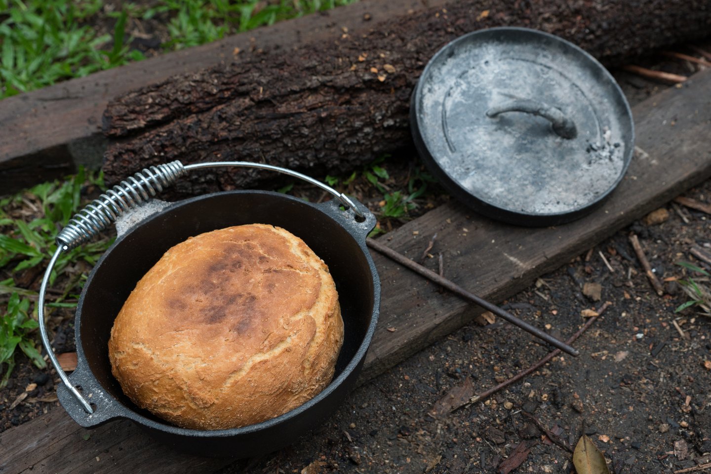 Cooked damper bread in a camp oven with the lid leaning against a log