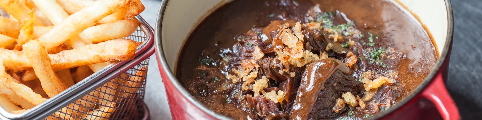 Flemish stew in a casserole dish with basket of French fries