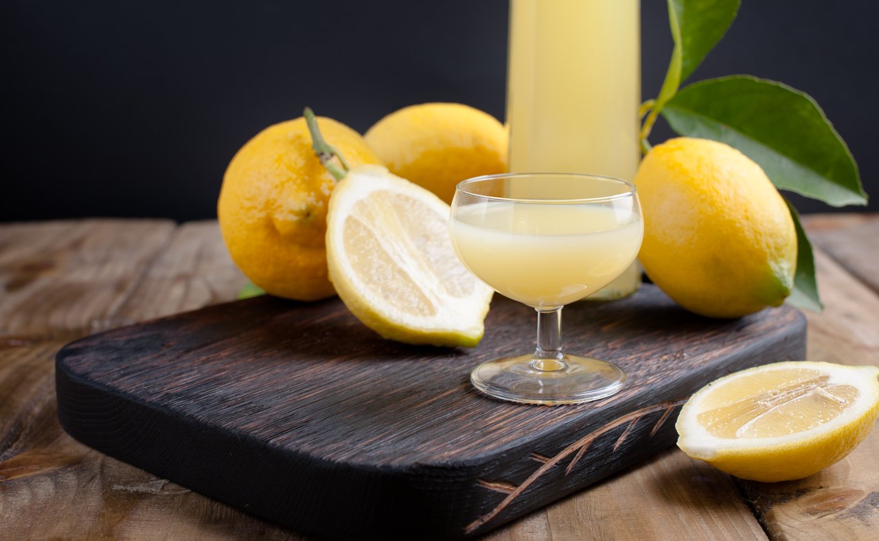 A glass of limoncello with lemons on a chopping board