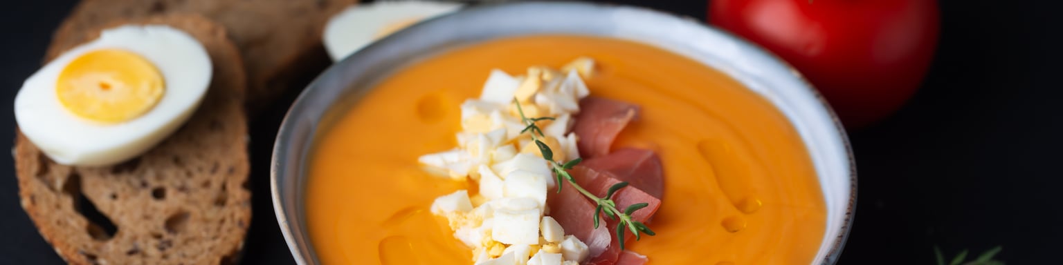 A bowl of salmorejo soup with the ingredients in the background