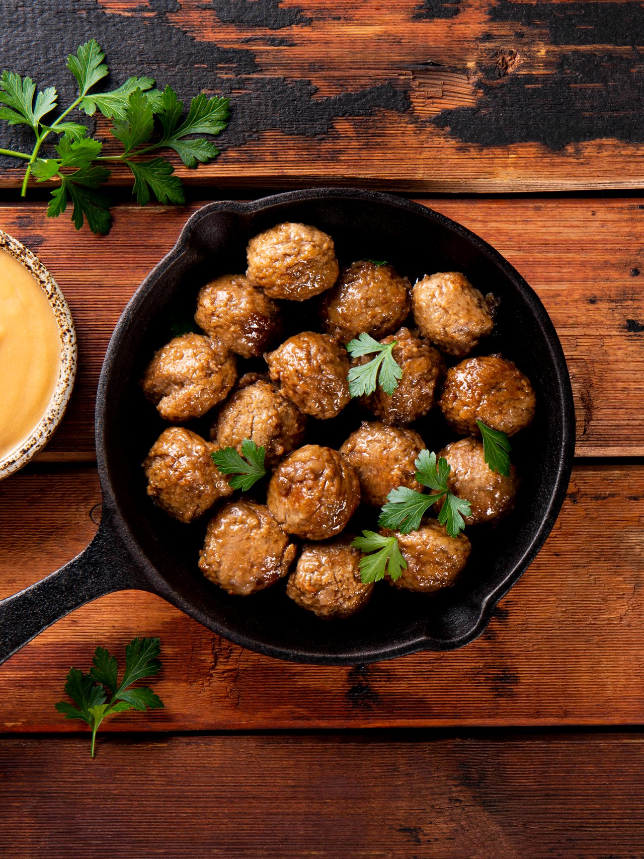 Swedish meatballs in a skillet with a dish of creamy brown sauce