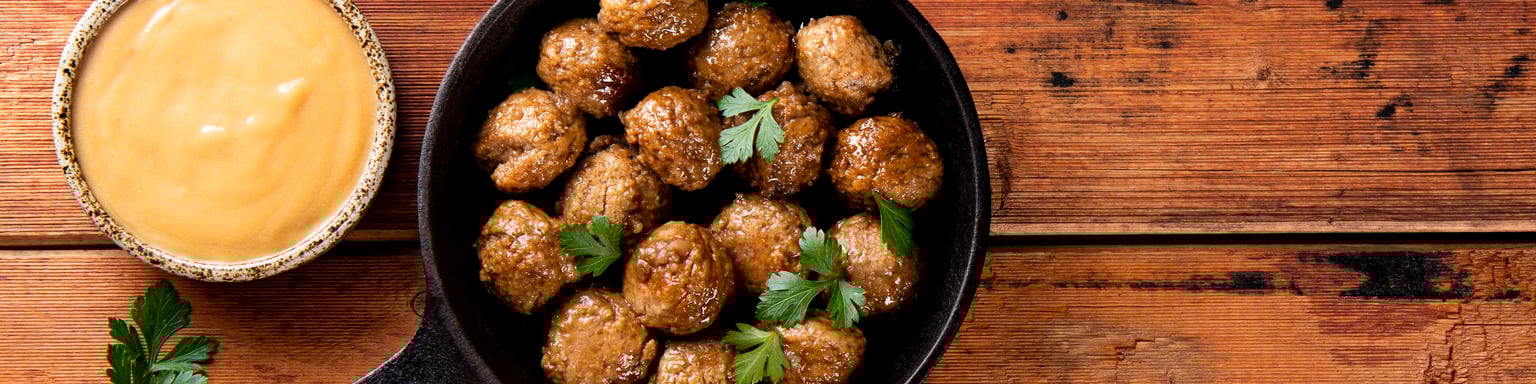 Swedish meatballs in a skillet with a dish of creamy brown sauce