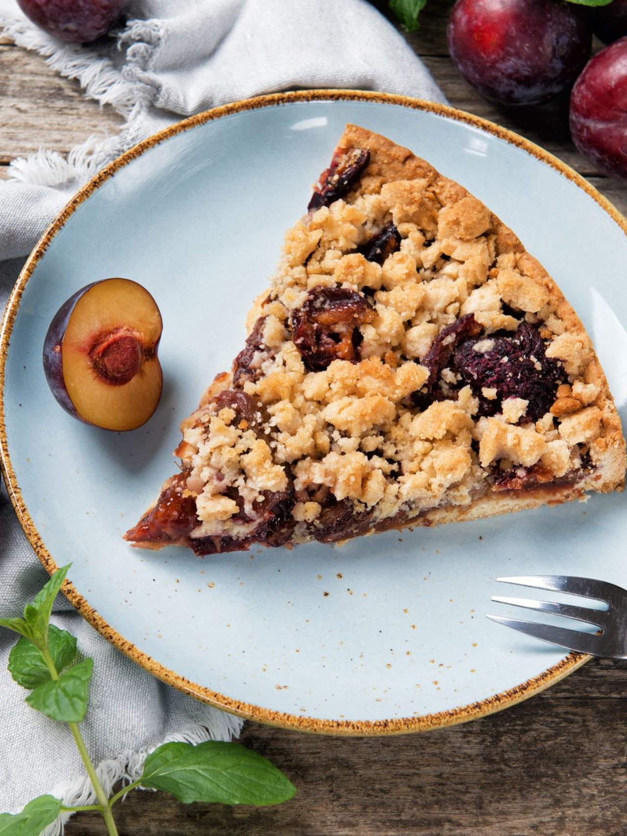 A piece of Zwetchgenkuchen on a plate with plum in the background