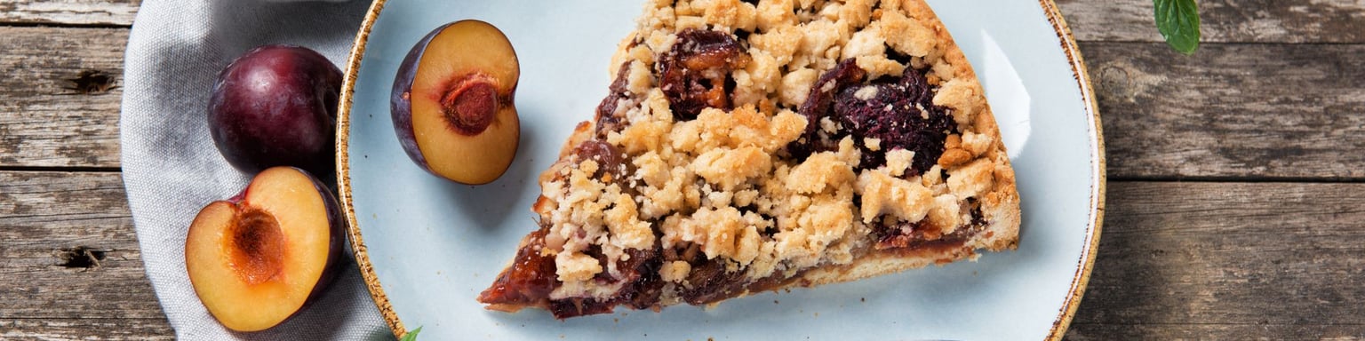 A piece of Zwetchgenkuchen on a plate with plum in the background