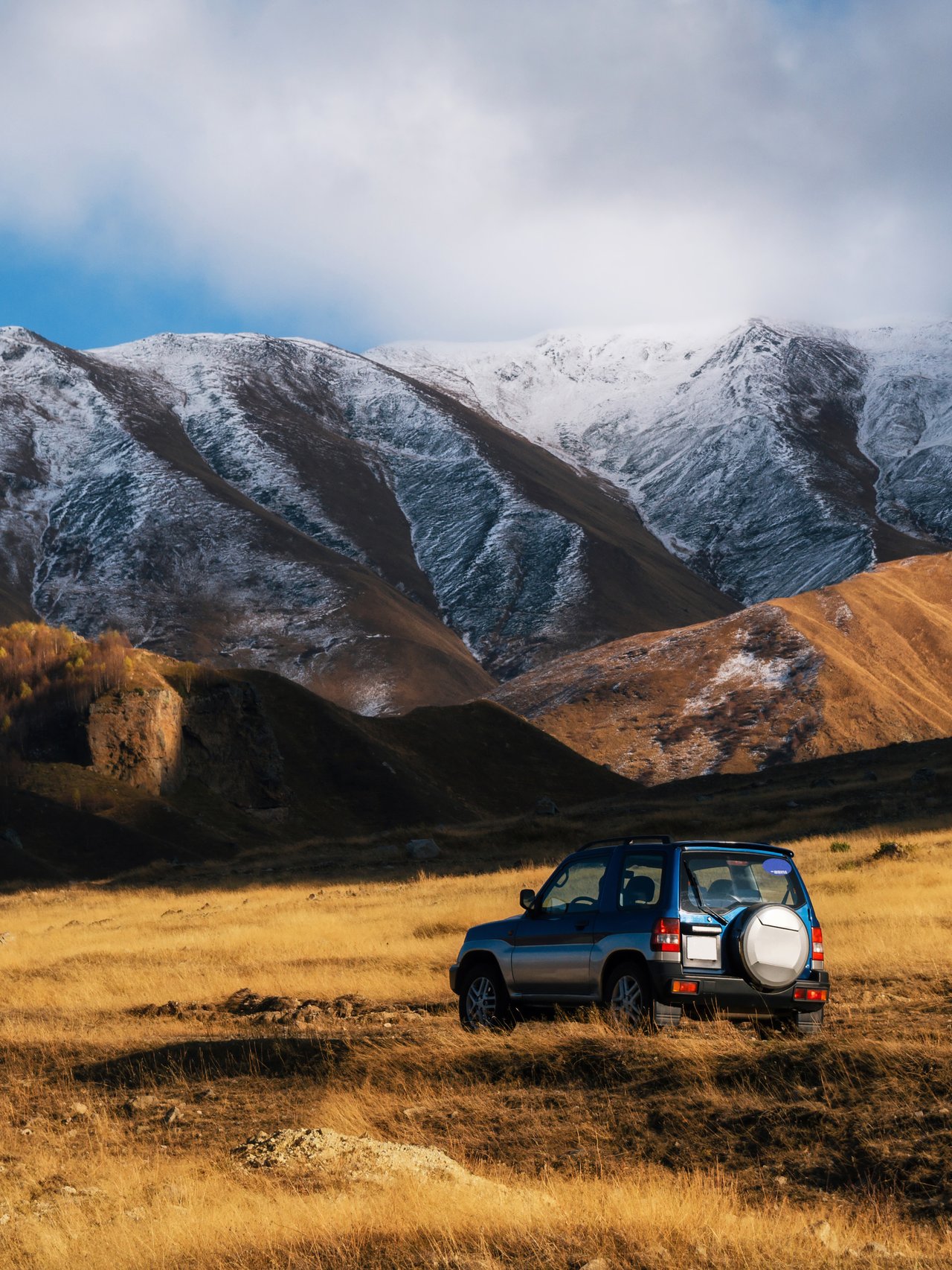 A blue 4WD jeep on a mountain road in Georgia with snowy peaks in the background.