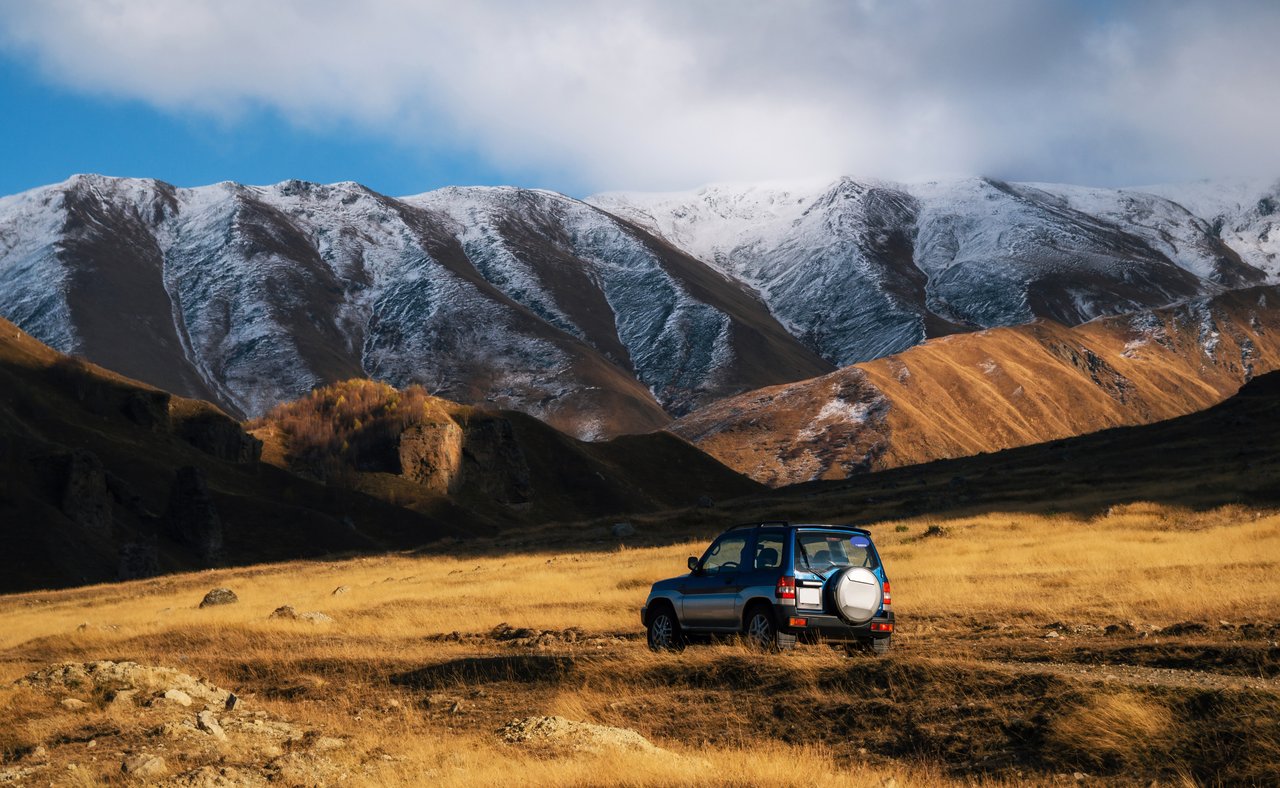 A blue 4WD jeep on a mountain road in Georgia with snowy peaks in the background.