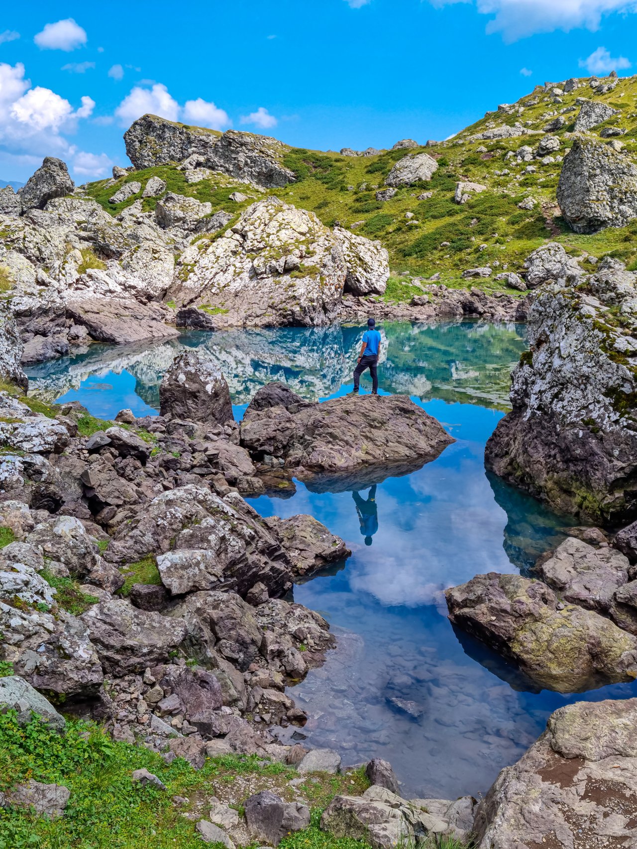 A hiker balancing on a rock reflected in one of the Abudelauri Lakes in Georgia