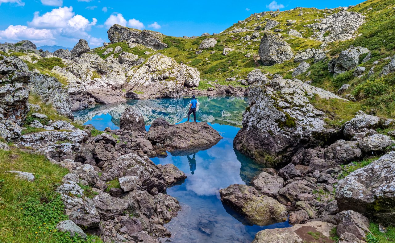 A hiker balancing on a rock reflected in one of the Abudelauri Lakes in Georgia