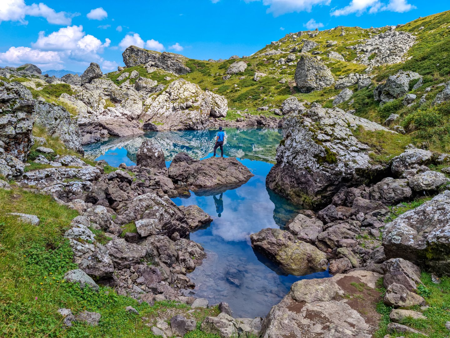 A hiker balancing on a rock reflected in one of the Abudelauri Lakes in Georgia