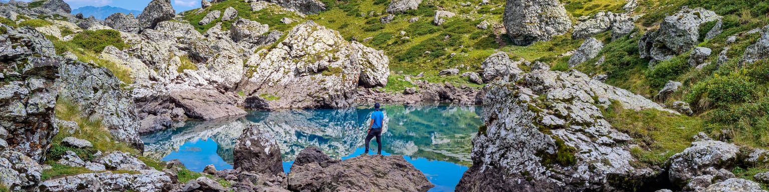 A hiker balancing on a rock reflected in one of the Abudelauri Lakes in Georgia