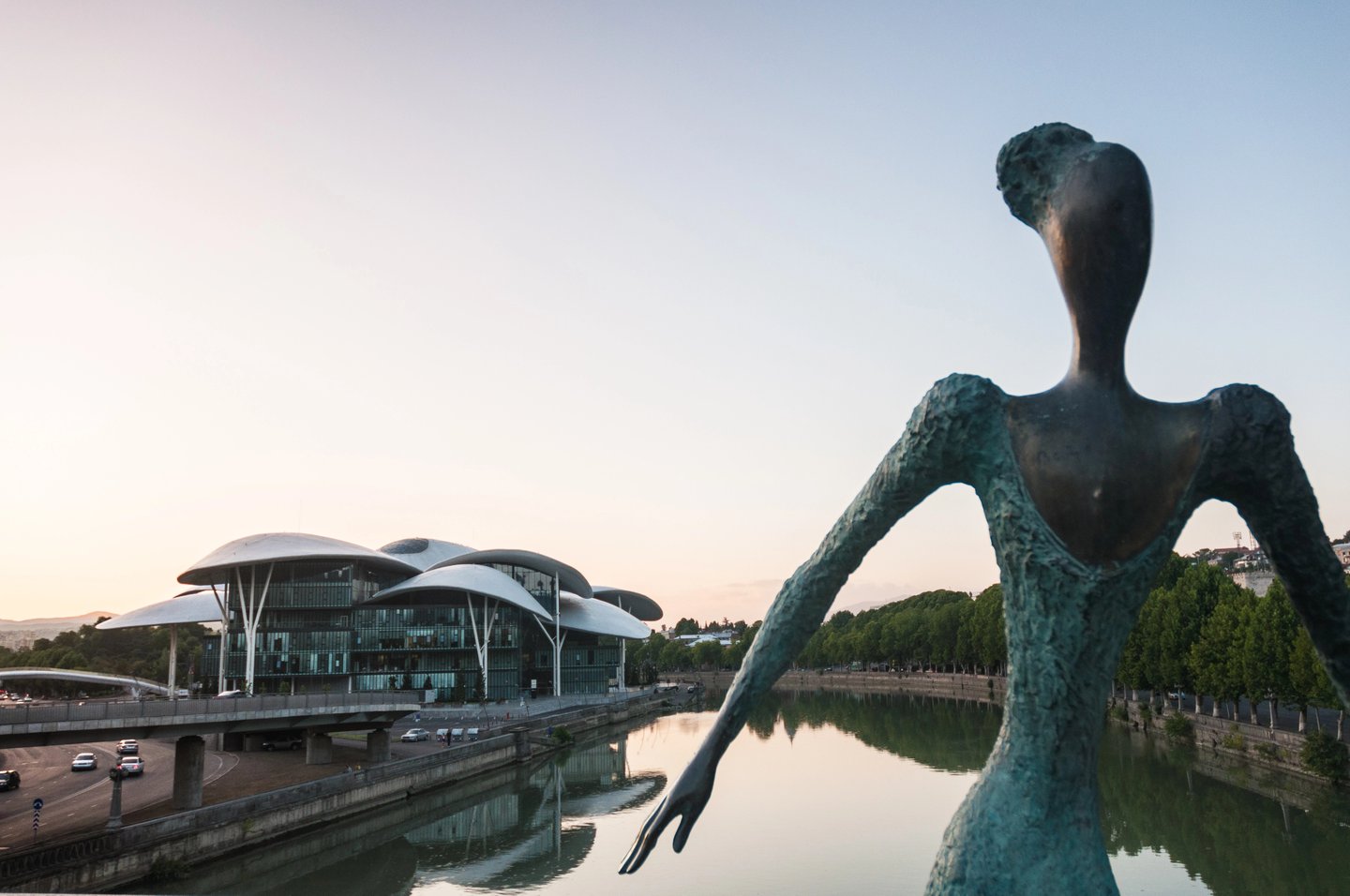 Looking across the river at the mushroom-like architecture of Tbilisi Public Service Hall with a sculpture in the foreground