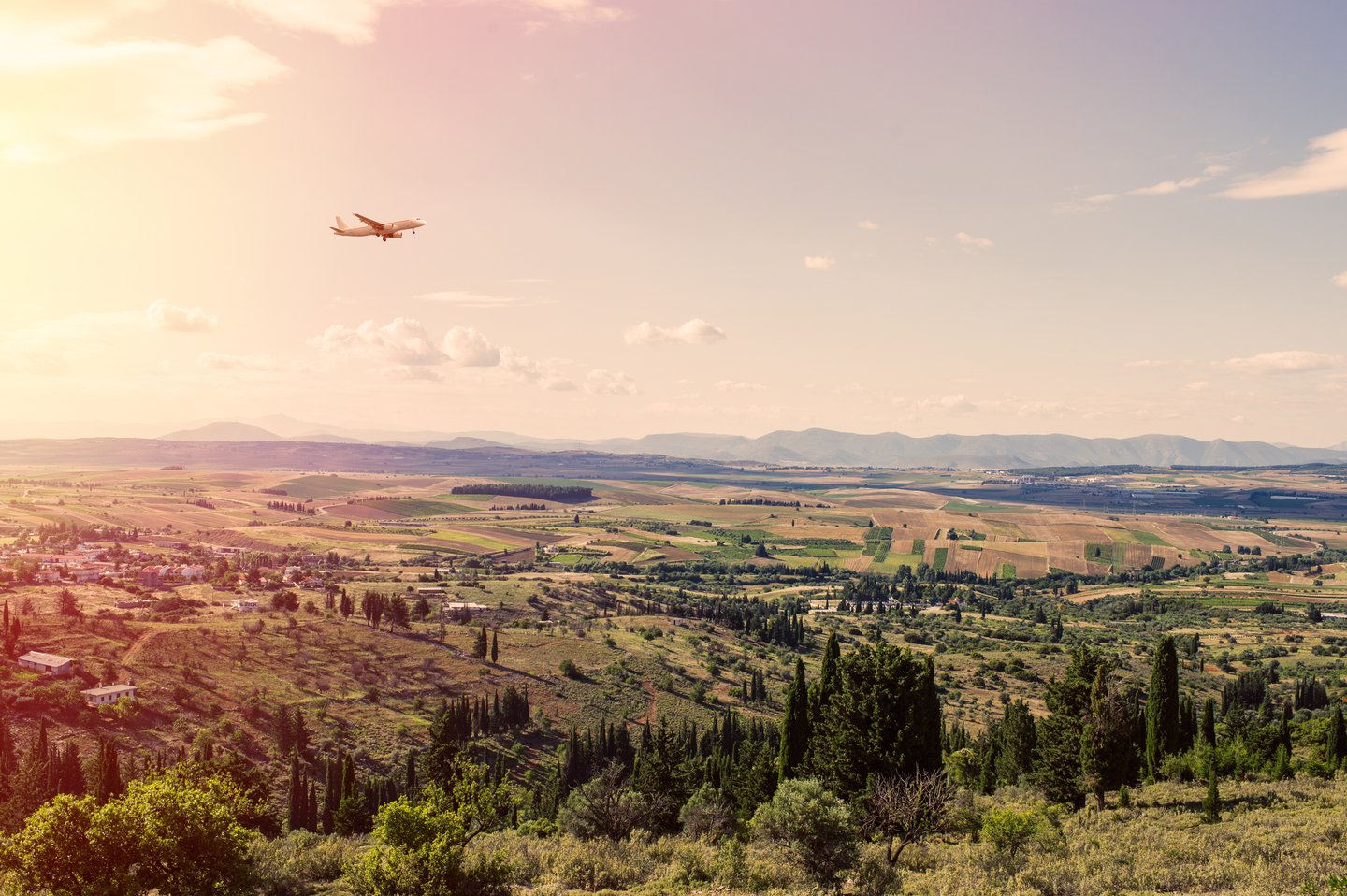 A plane landing at sunset over semi-rural Athens.