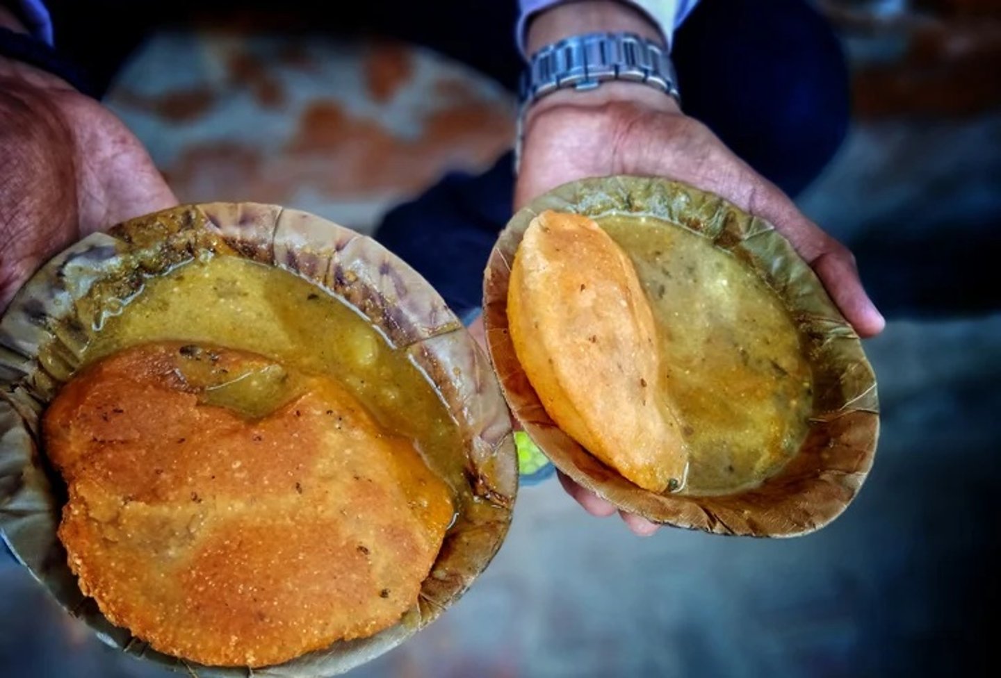 A woman holding out plates of Kachori Sabji in India