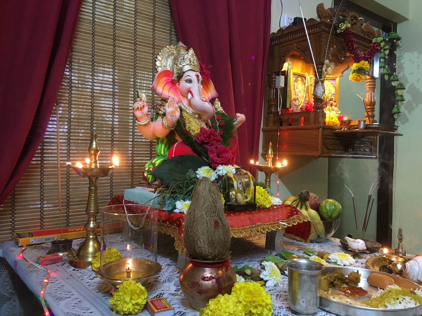 A Ganesh idol surrounded by lamps, flowers, incense and food