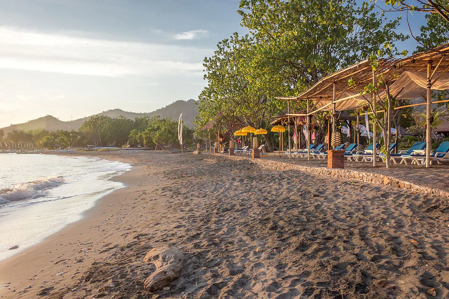 Peaceful Pemuteran Beach with a few loungers and umbrellas and trees in the background