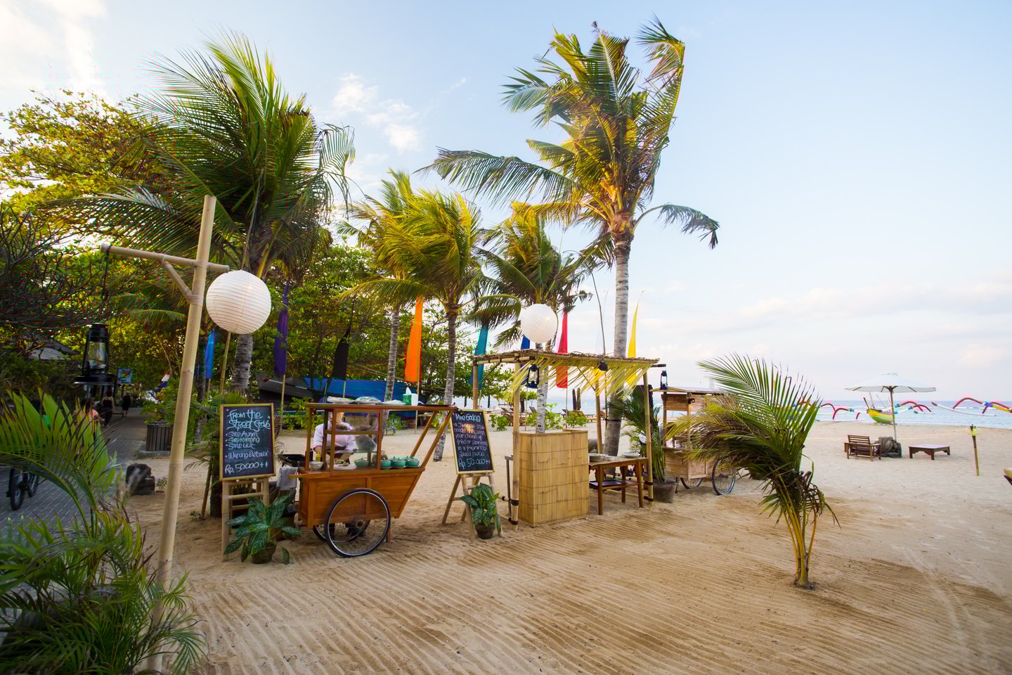 Palm trees, fruit vendor and umbrellas on a sandy beach in Sanur, Bali