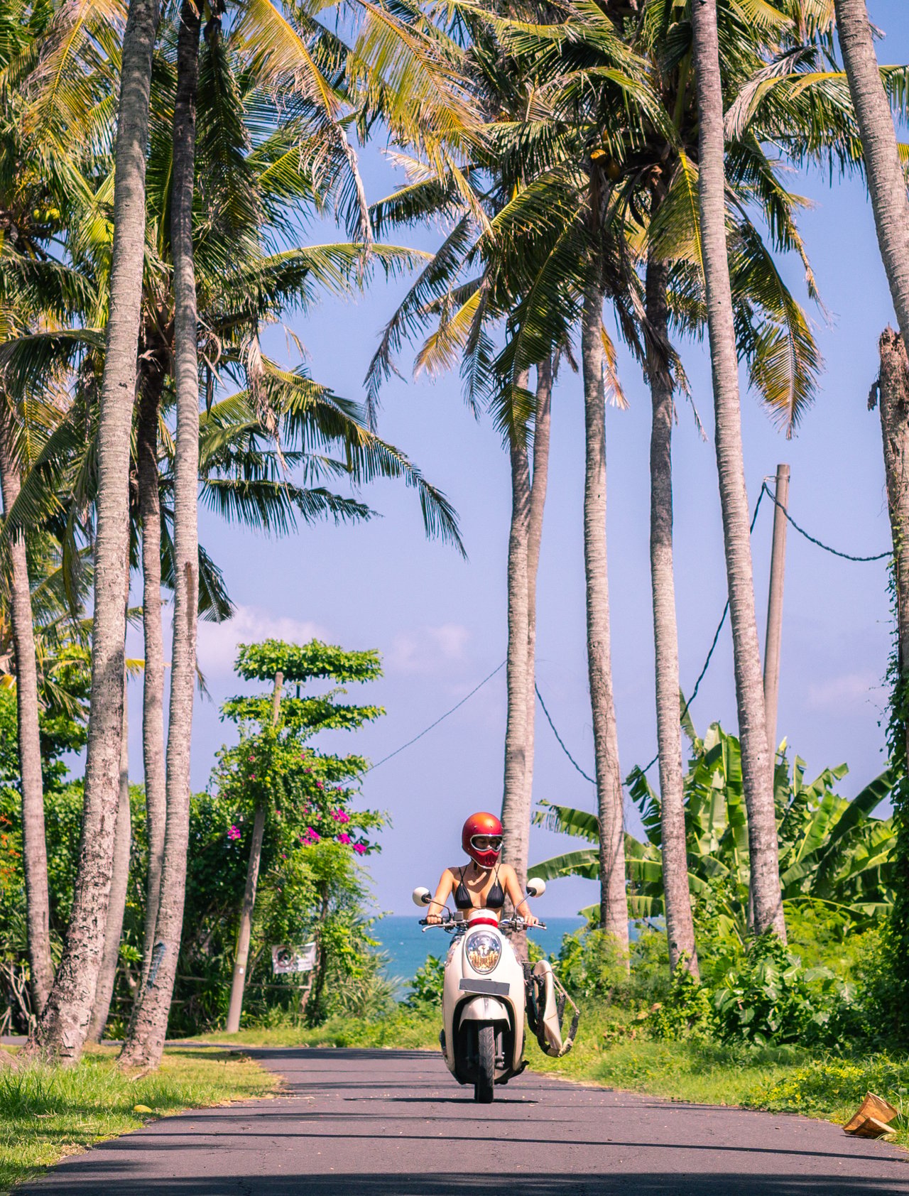 A young woman riding a scooter between palm trees in Bali.