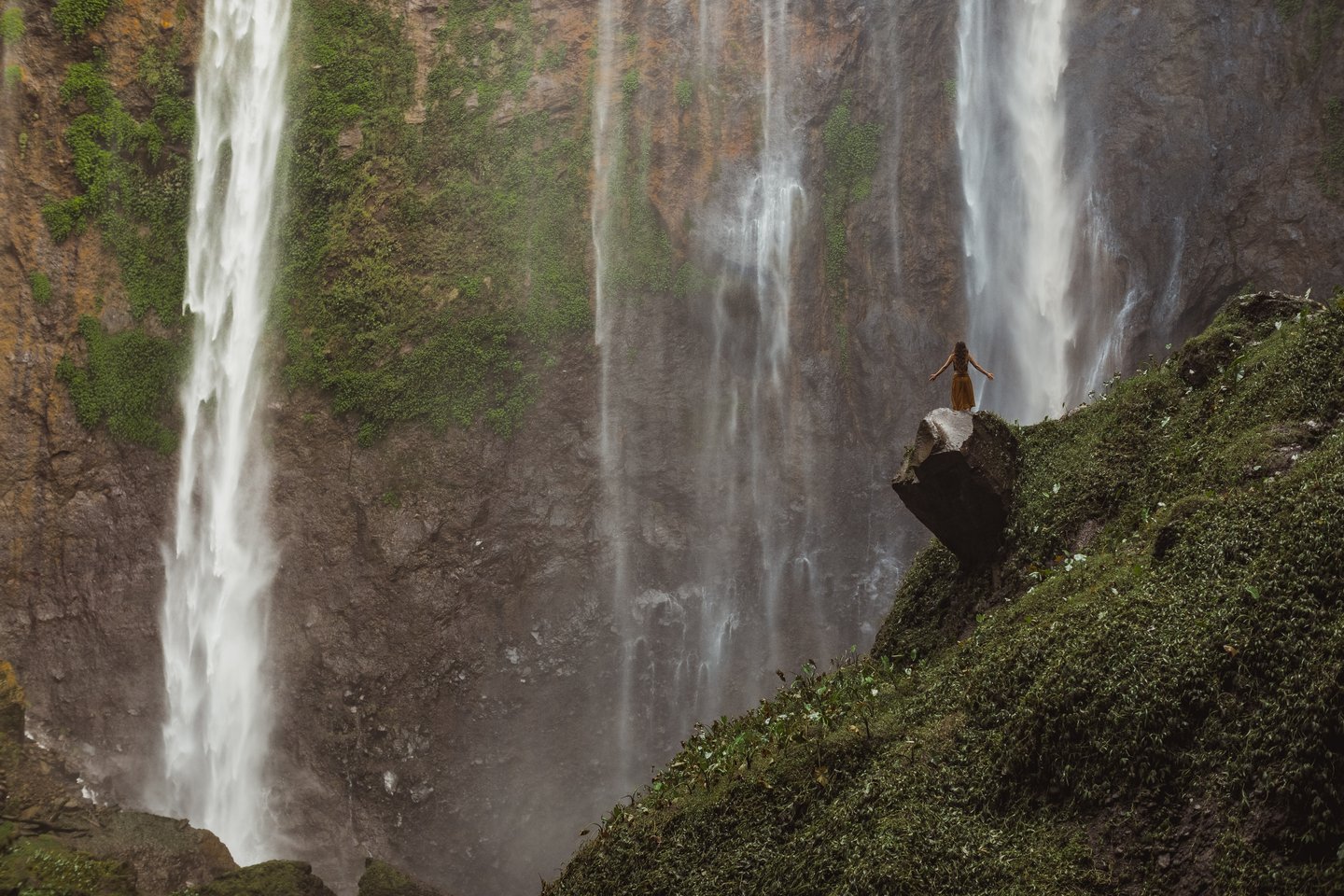 A woman on a rock in front of the Tumpak Sewu waterfalls 
