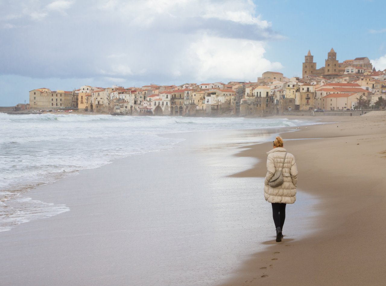 Solitary woman walking the beach of Cefalu in winter time, Sicily,