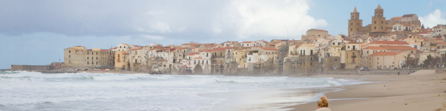 Solitary woman walking the beach of Cefalu in winter time, Sicily,