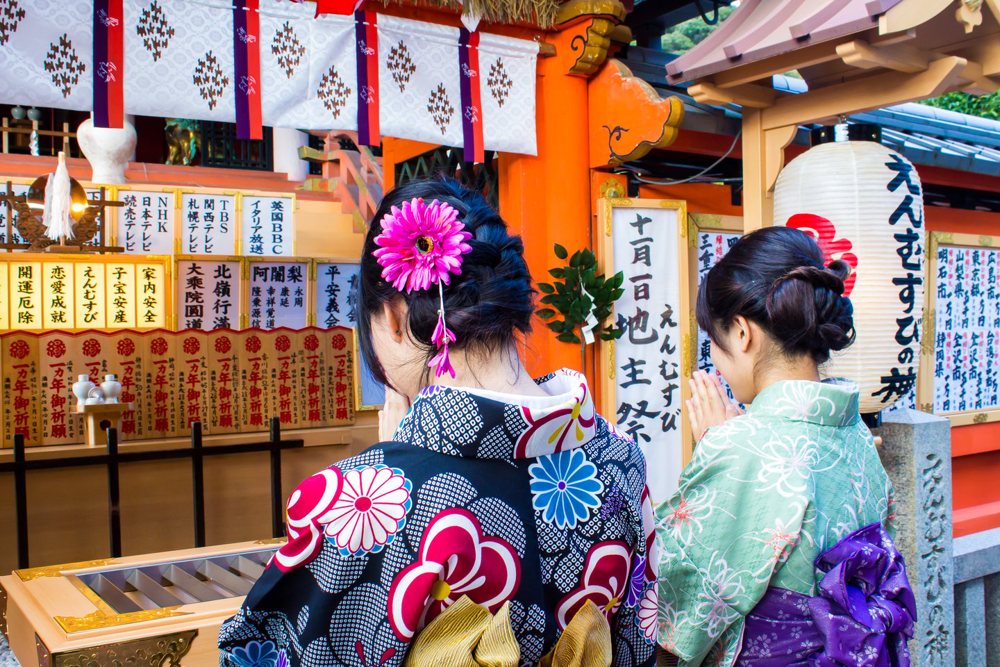 Two Japanese girls dressed with colourful kimonos praying in a shrine.