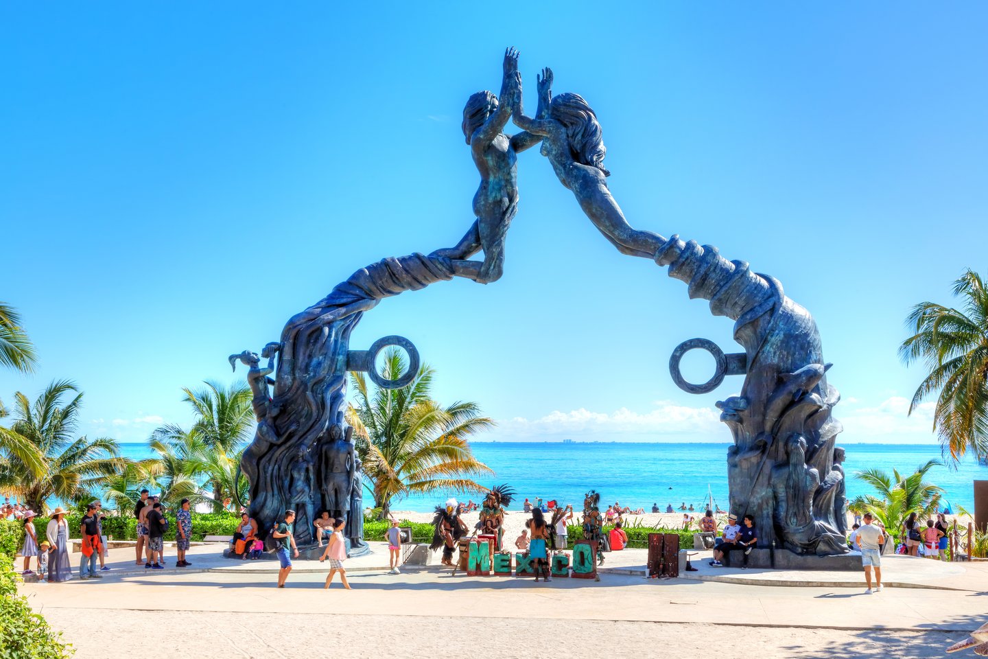 Visitors mingling on Fundadores Park beach under the Portal Maya sculpture in Playa del Carmen