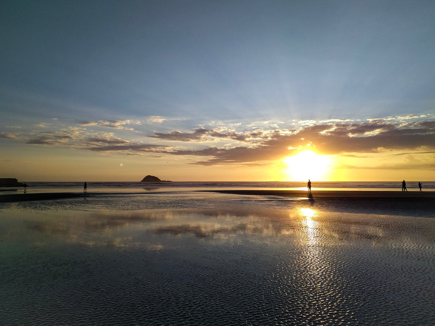 The sunset reflected in the water and black sand at Muriwai Beach, Auckland