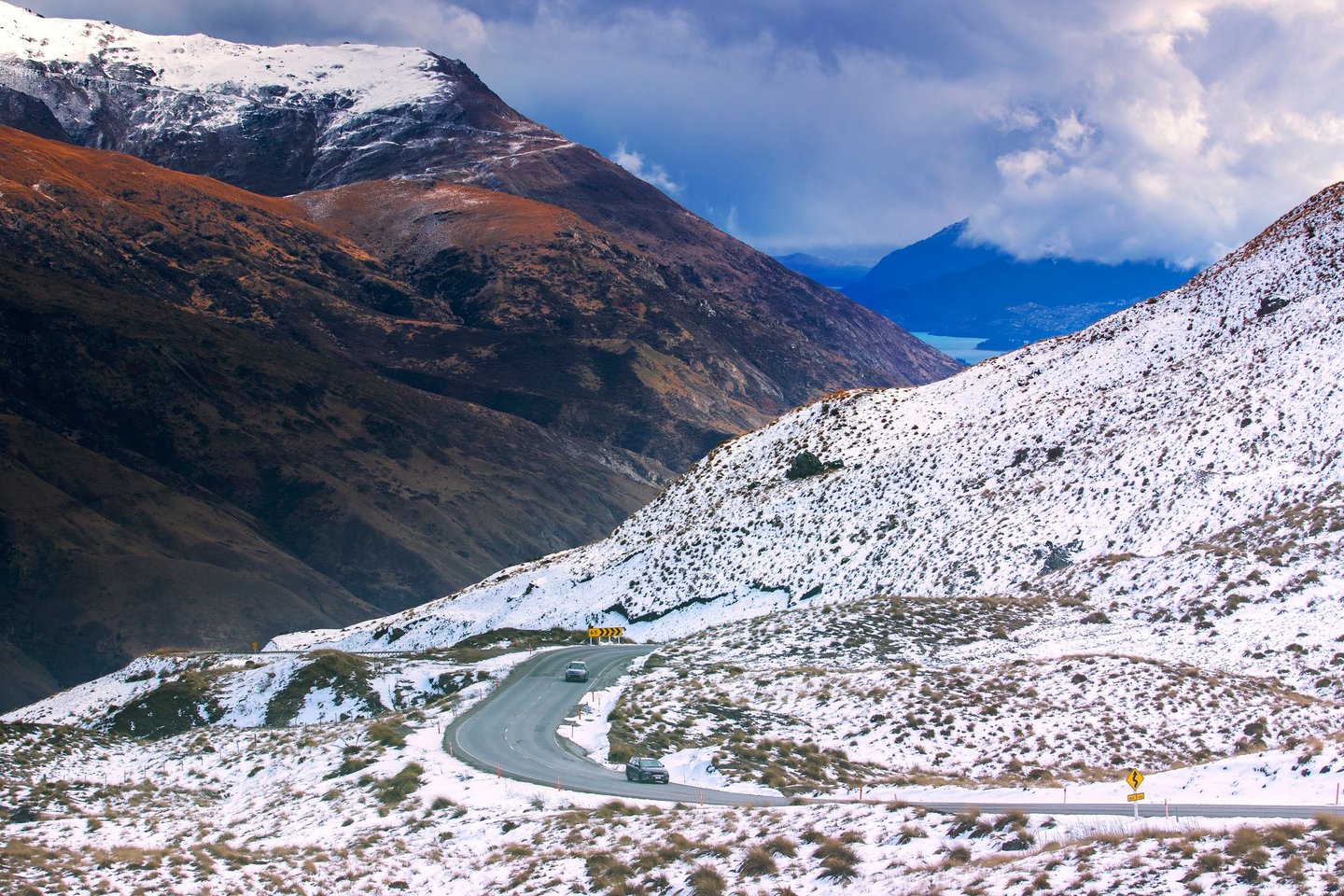 A car driving between snowy mountains on the Crown Range road