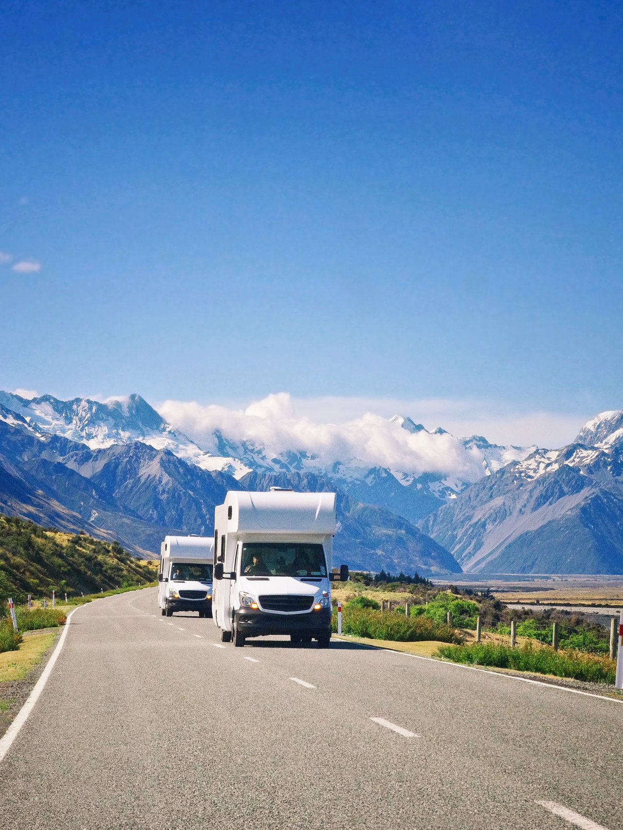 Two campervans driving down the road with mountains in the background