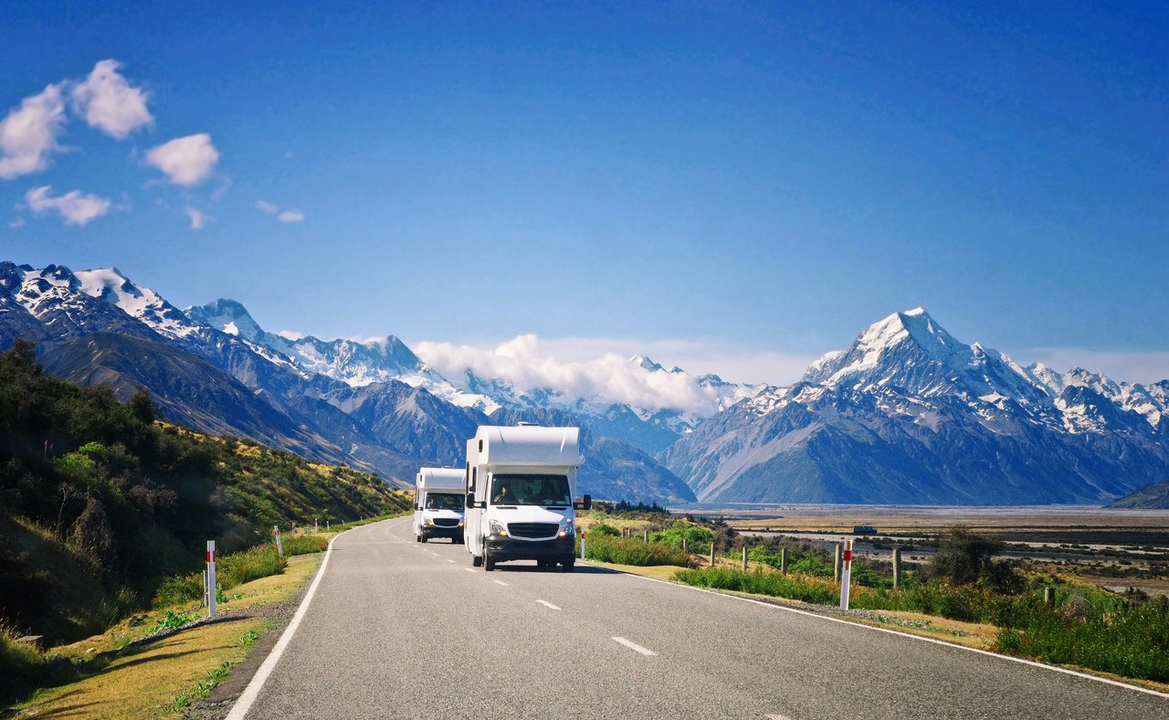 Two campervans driving down the road with mountains in the background