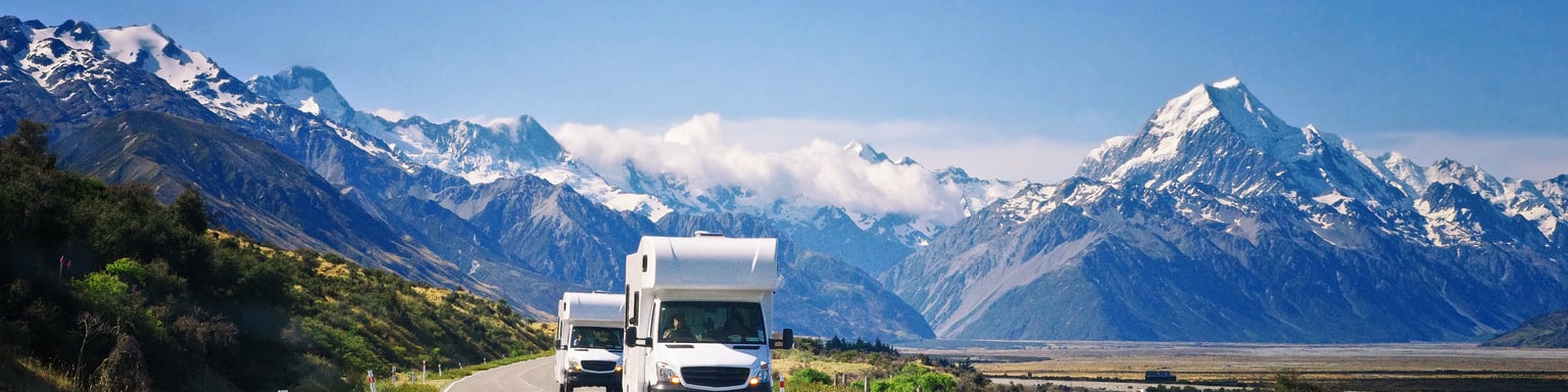 Two campervans driving down the road with mountains in the background