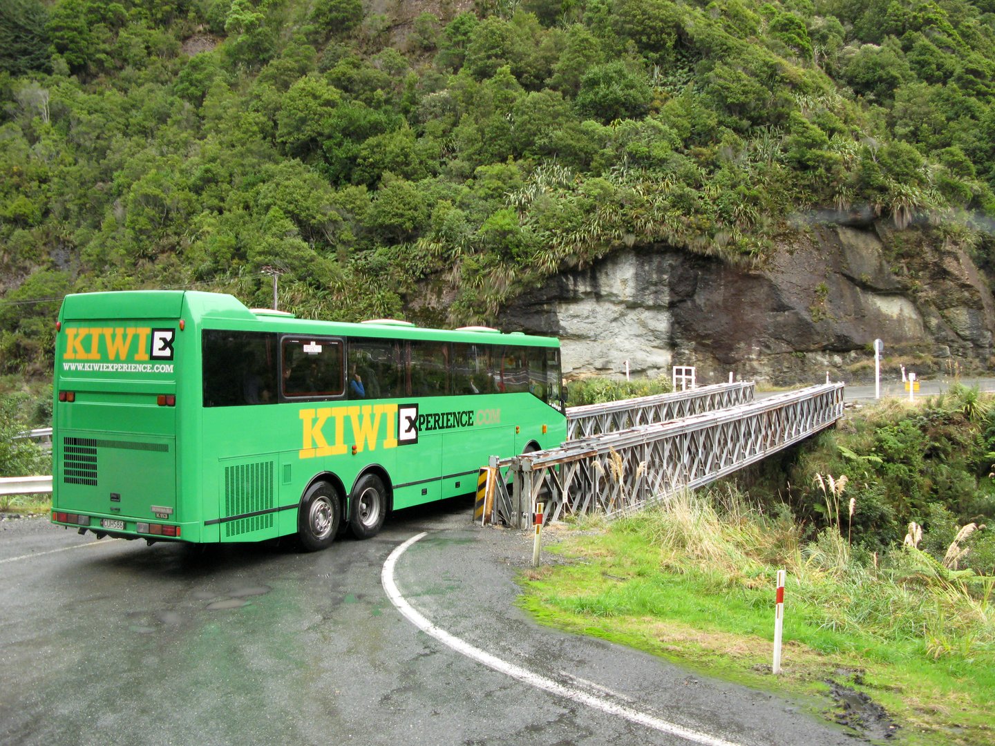 A green Kiwi Experience bus crossing a bridge in Te Wahipounamu, New Zealand