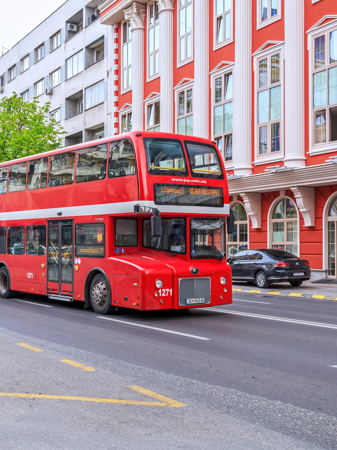 A red bus driving down the street in Skopje, North Macedonia.