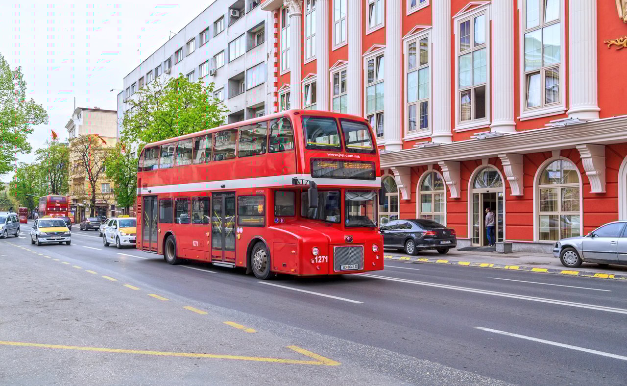 A red bus driving down the street in Skopje, North Macedonia.
