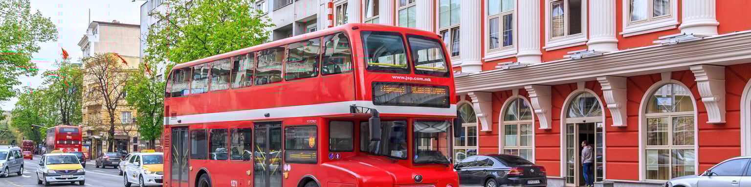 A red bus driving down the street in Skopje, North Macedonia.