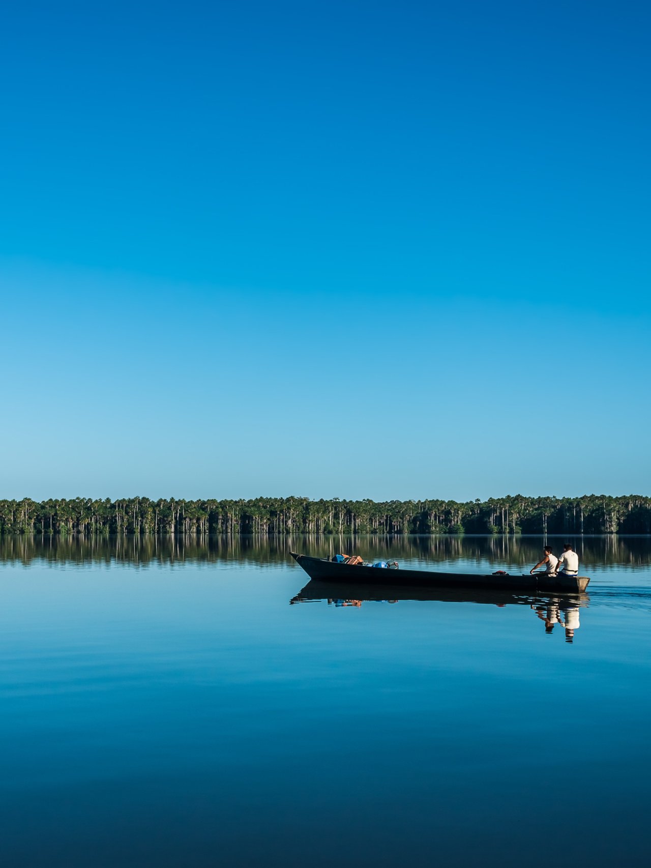 People on boat with a blue sky and water in the Amazon jungle at Madre de Dios, Peru