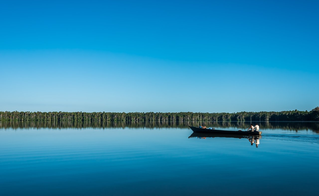People on boat with a blue sky and water in the Amazon jungle at Madre de Dios, Peru