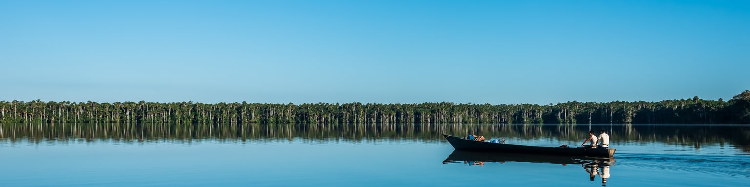 People on boat with a blue sky and water in the Amazon jungle at Madre de Dios, Peru