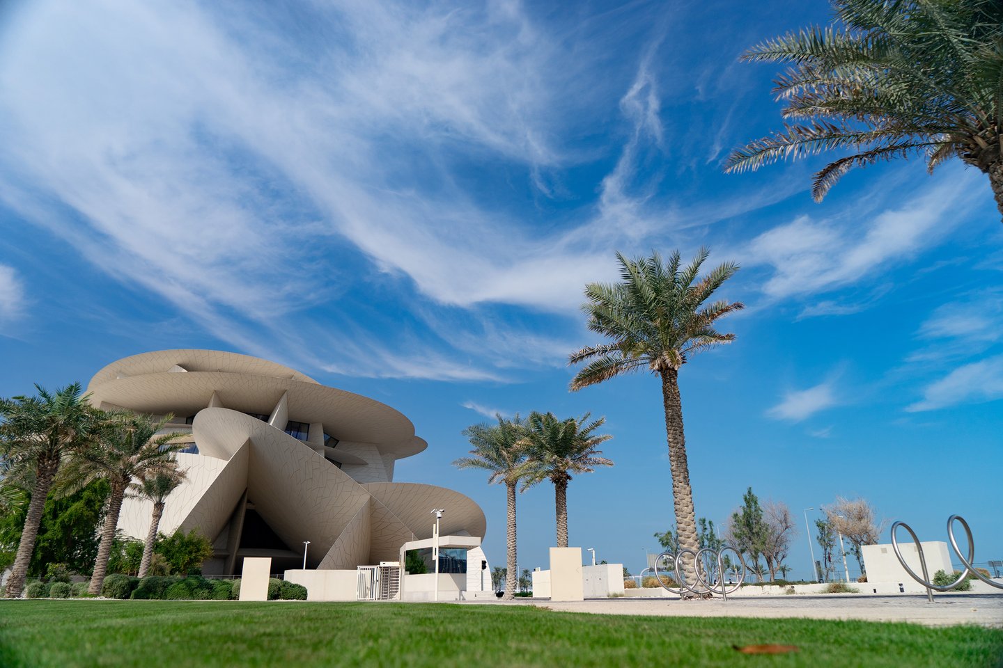 The National Museum of Qatar with palm trees and grass