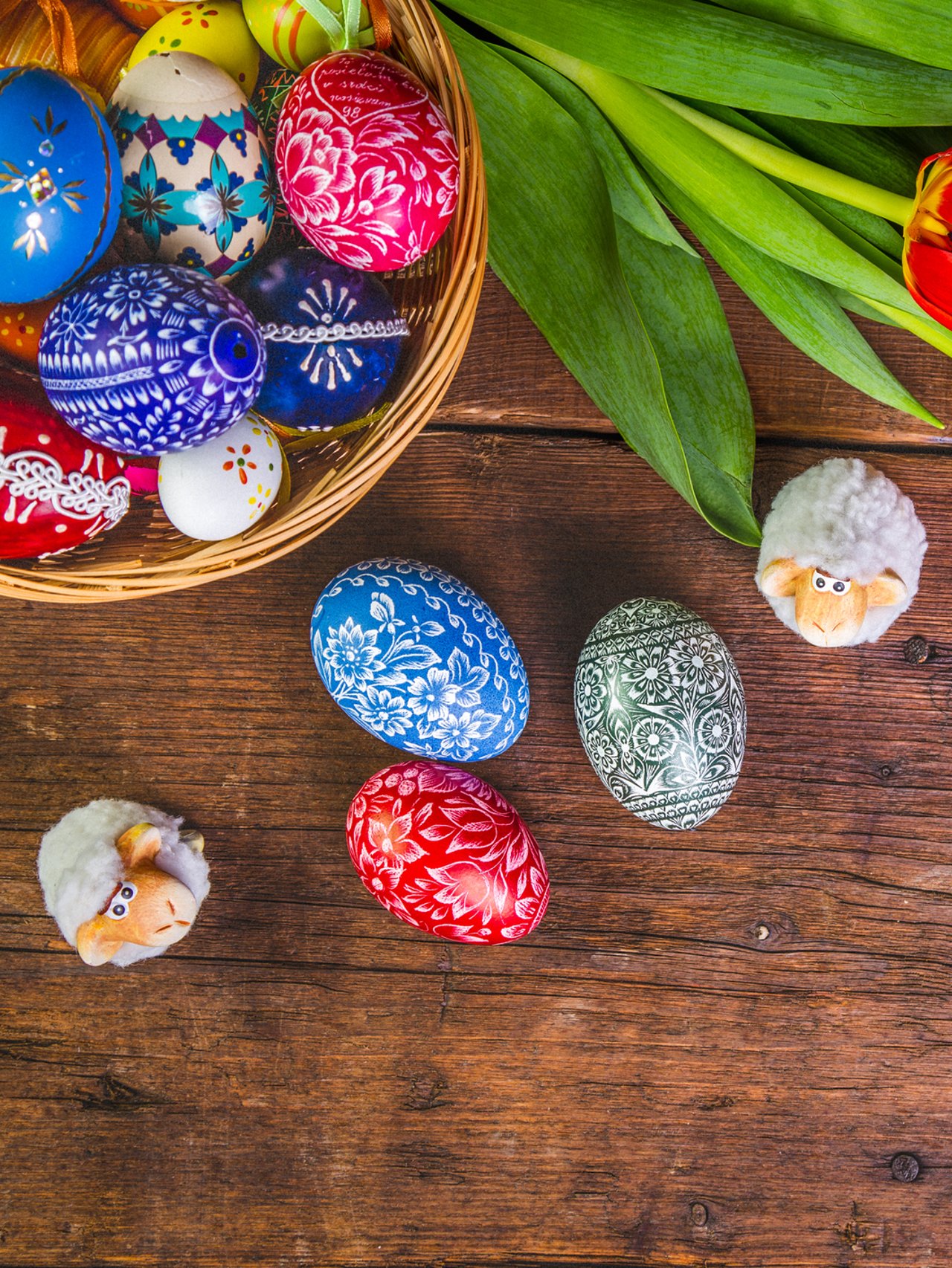 A basket of painted eggs with tulips and small, ornamental sheep