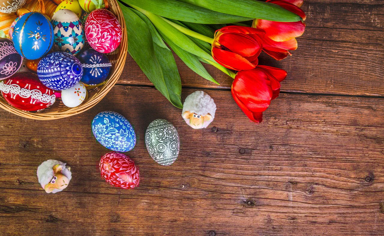 A basket of painted eggs with tulips and small, ornamental sheep