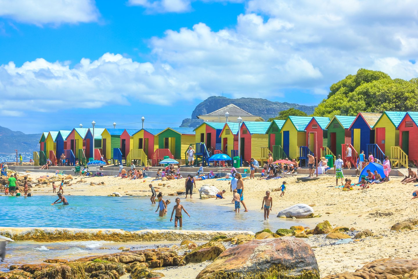 People playing in the sea outside the colourful beach huts on Muizenberg Beach in Cape Town, South Africa.