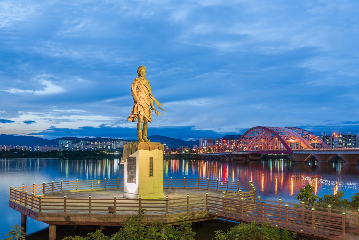 Chuncheon's statue with the city and bridge lit up in the background.