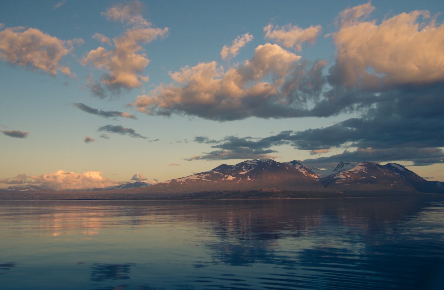 Calm Lake Akkajaure at sunset with snow covered mountains in background