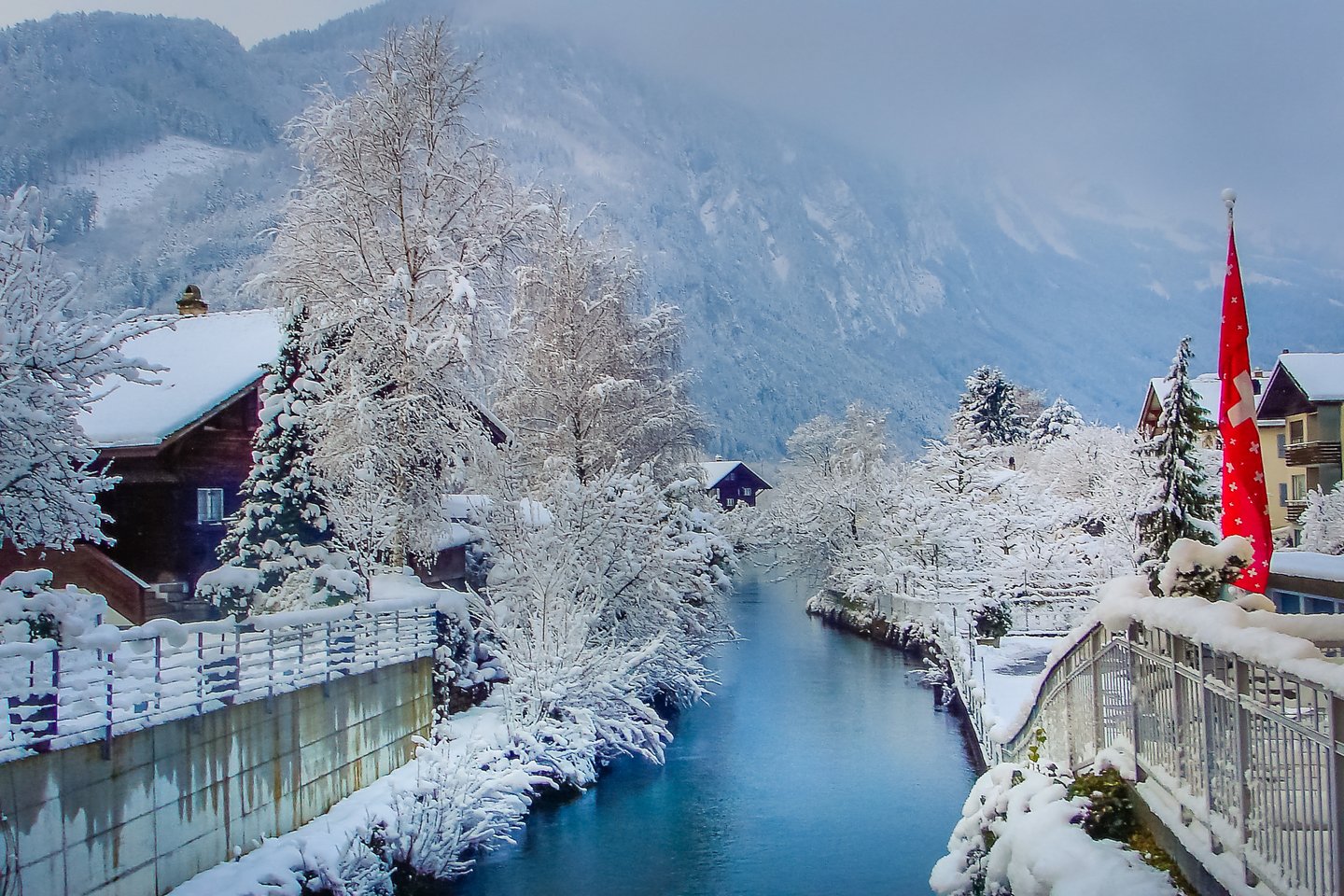 Snow-covered houses and trees along a river in Interlaken, Switzerland