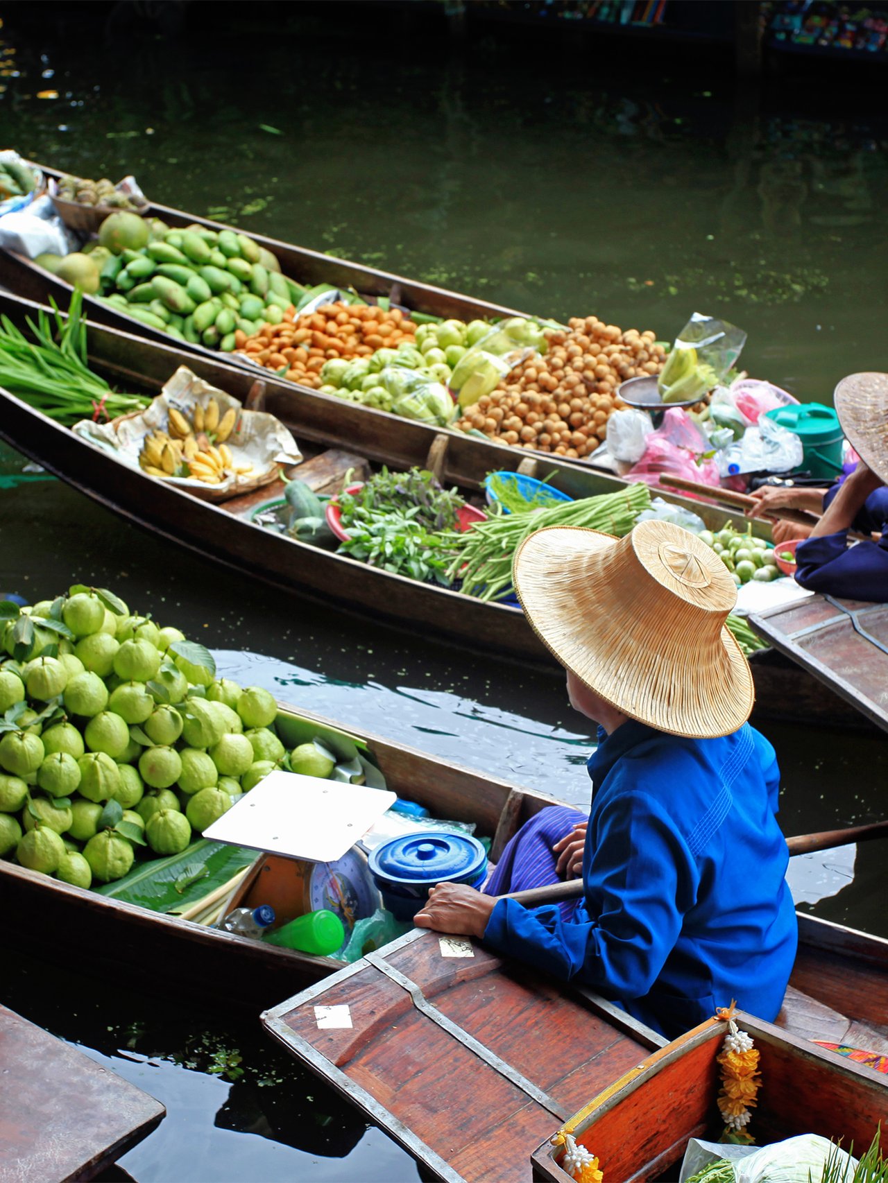 Vendors selling fruit and vegetables at a floating market in Thailand.