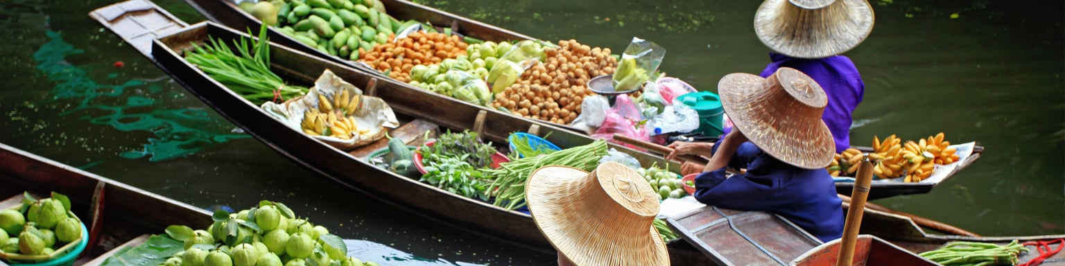 Vendors selling fruit and vegetables at a floating market in Thailand.