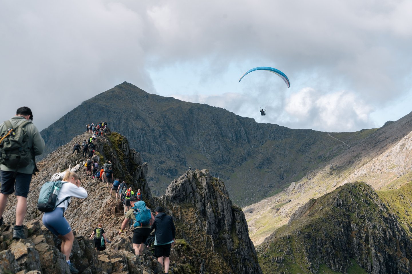 Hikers on their way up the vertiginous Crib Goch, with a paraglider overhead