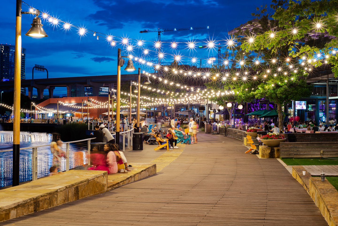 People eating at restaurants along a boardwalk with fairy lights