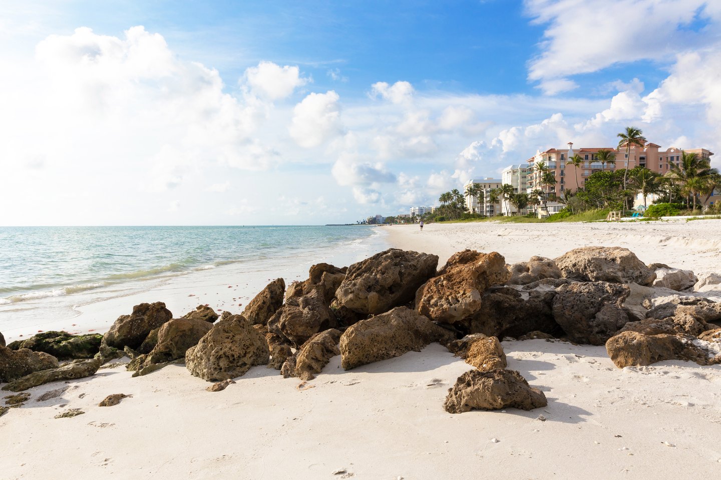 A white, sandy beach with rocks in the foreground in Naples, Florida